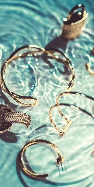 Gouden armbanden, oorbellen, ringen, sieraden op smaragd water bac — Stockfoto