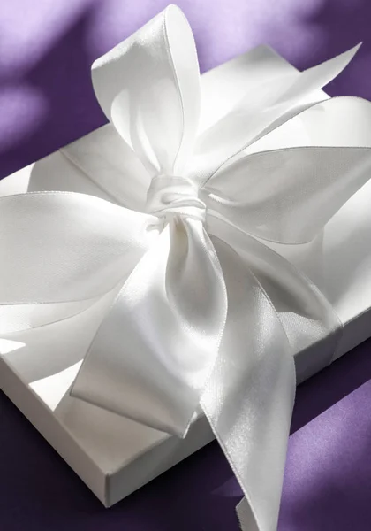 豪华节日白色礼品盒，带丝带，在紫罗兰上鞠躬 — 图库照片