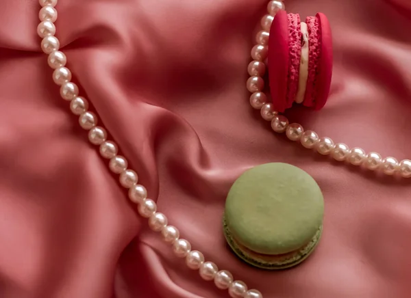 Sweet macaroons and pearls jewellery on silk background, parisia