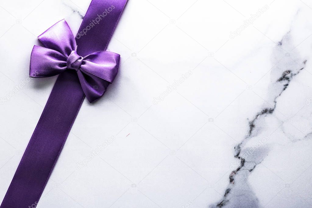 Purple silk ribbon and bow on luxury marble background, holiday 