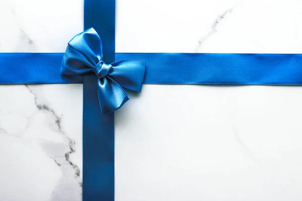 Blue silk ribbon and bow on luxury marble background, holiday fl