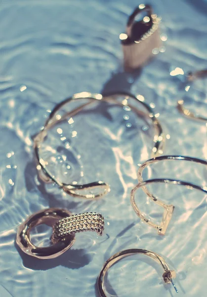 Gouden armbanden, oorbellen, ringen, sieraden op blauw water backgr — Stockfoto