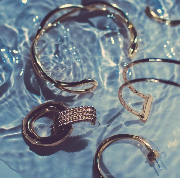 Arany karkötők, fülbevalók, gyűrűk, ékszerek kék víz backgr — Stock Fotó