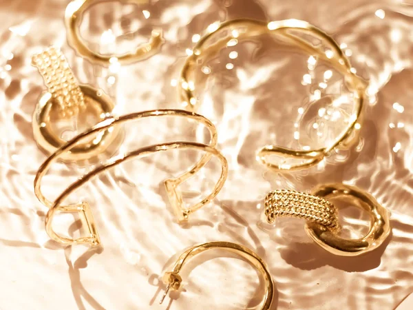 Pulseiras douradas, brincos, anéis, jóias em backgr água de ouro — Fotografia de Stock