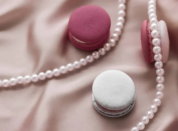 Sweet macaroons and pearls jewellery on silk background, parisia