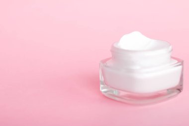 Pembe arka planda yüz kremi nemlendirici kavanozu, nemlendirici cilt