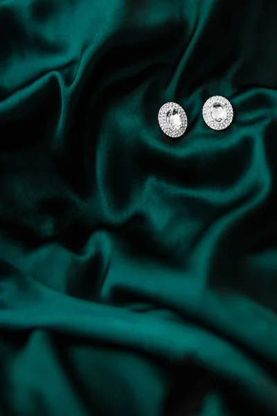 Luxusní diamantové náušnice na tmavě smaragdově zeleném hedvábí, sváteční glám — Stock fotografie