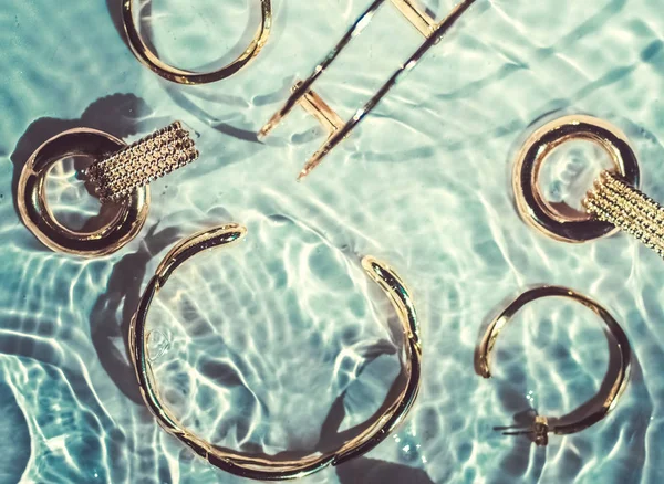 Golden bracelets, earrings, rings, jewelery on emerald water bac