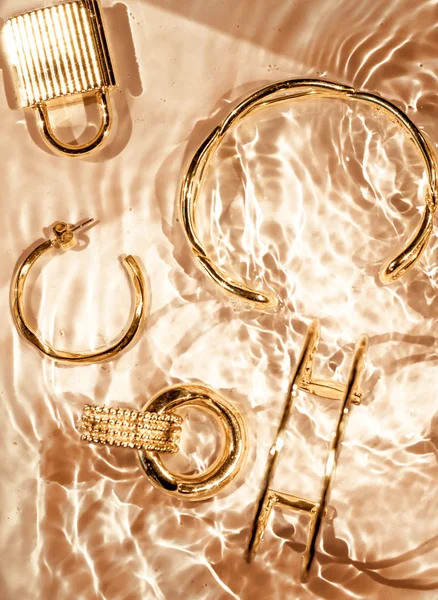 Golden bracelets, earrings, rings, jewelery on gold water backgr