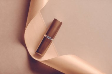 Bej rengi tatil arkaplanında lüks ruj ve ipek kurdele, mak