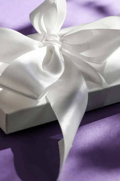 Розкішна святкова біла подарункова коробка з шовковою стрічкою та бантом на фіолетовому — стокове фото