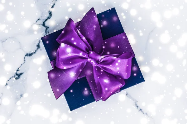 Zima wakacje pudełko z fioletowym jedwabnym łukiem, śnieg brokat na ma — Zdjęcie stockowe