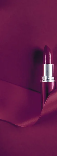 Luxury lipstick and silk ribbon on plum holiday background, make