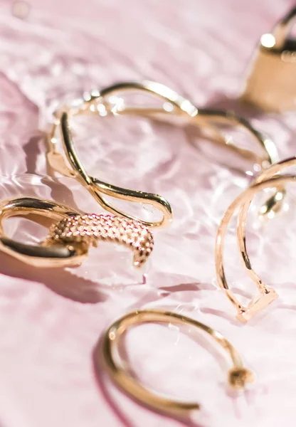 Goldene Armbänder, Ohrringe, Ringe, Schmuck auf rosa Wasserrücken — Stockfoto