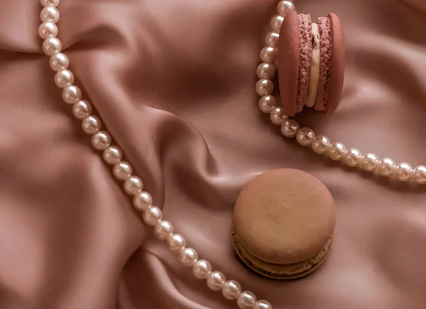 Sweet macaroons and pearls jewellery on silk background, parisia
