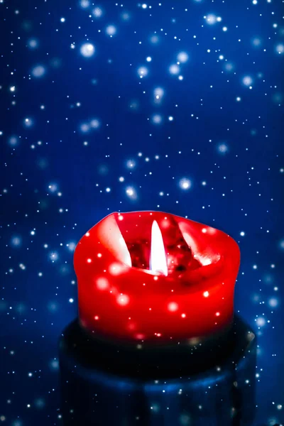 Red holiday candle on blue sparkling snowing background, luxury