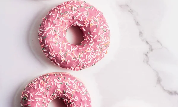 Frosted sprinkled donuts, sweet pastry dessert on marble table b — Stock Photo, Image