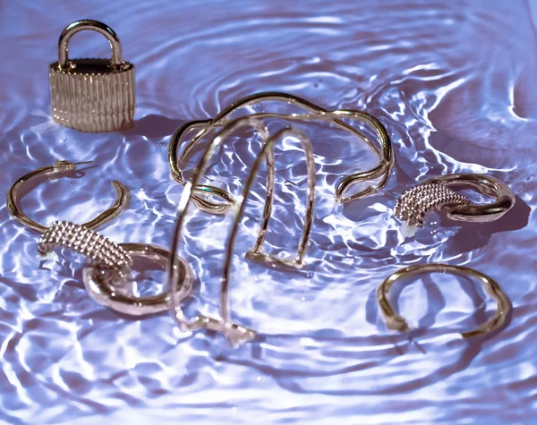 Gouden armbanden, oorbellen, ringen, sieraden op paars water terug — Stockfoto