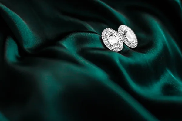Luxury diamond earrings on dark emerald green silk, holiday glam