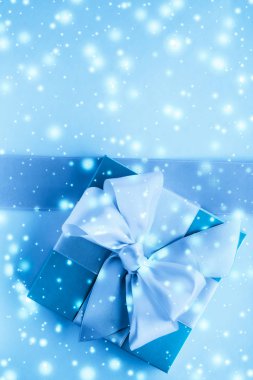 Kış tatili hediyeleri ve dondurulmuş mavi arka planda parlayan kar,