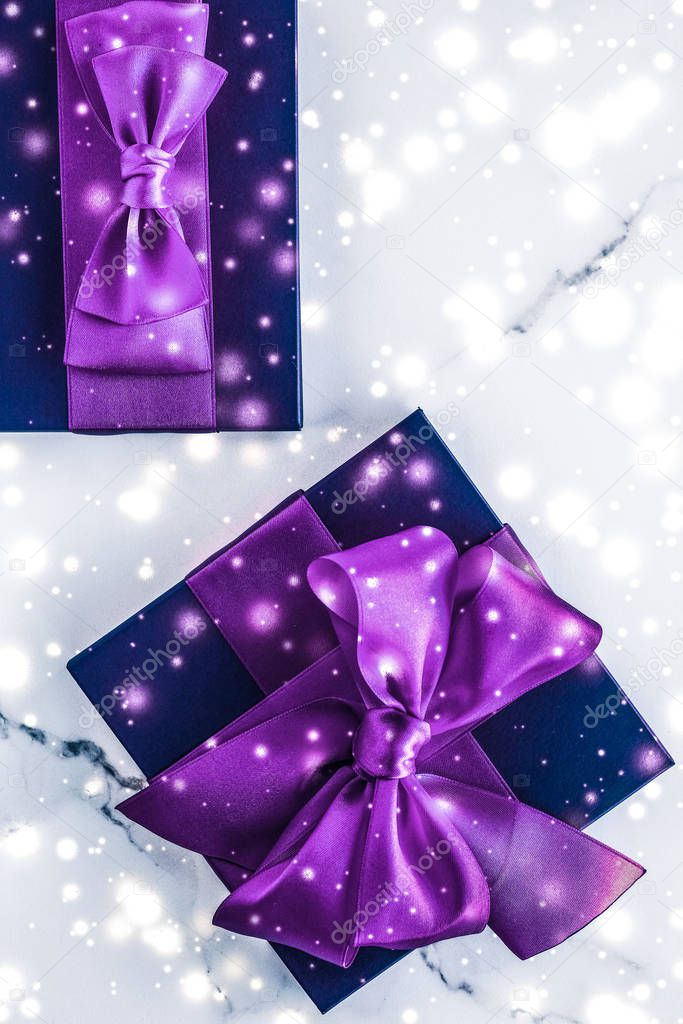 Winter holiday gift box with purple silk bow, snow glitter on ma