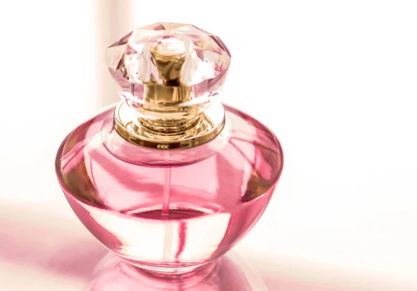 Pink perfume bottle on glossy background, sweet floral scent, gl