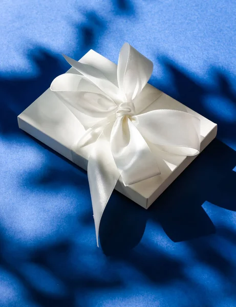 Розкішна святкова біла подарункова коробка з шовковою стрічкою та бантом на синьому б — стокове фото