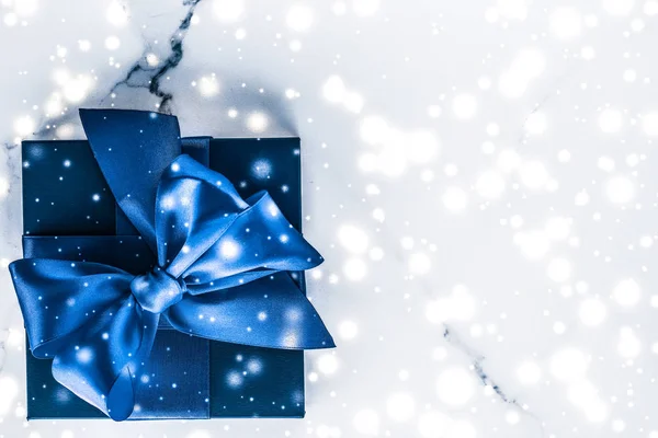 Winter holiday gift box with blue silk bow, snow glitter on marb