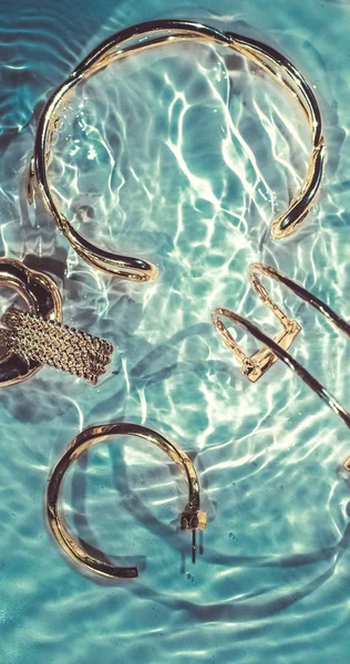 Gouden armbanden, oorbellen, ringen, sieraden op smaragd water bac — Stockfoto