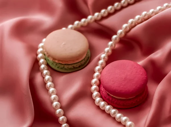 Sweet macaroons and pearls jewellery on silk background, parisia