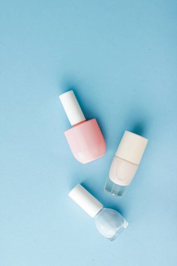 Mavi arka planda renkli tırnak cilası şişeleri, güzellik markası için organik makyaj malzemeleri ve kozmetik ürünleri.