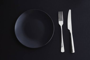 Siyah arka planda boş tabaklar ve gümüş takımlar, bayram yemeği için özel sofra takımı, minimal tasarım ve diyet