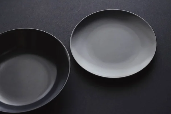 Assiettes vides sur fond noir, vaisselle haut de gamme pour le dîner de vacances, design minimaliste et régime alimentaire — Photo