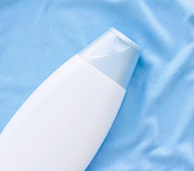 Mavi ipek arka planda boş etiket şampuan şişesi veya duş jeli modeli, güzellik ürünü ve vücut bakımı kozmetiği