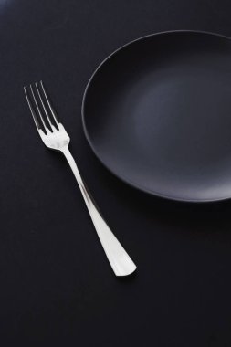 Siyah arka planda boş tabaklar ve gümüş takımlar, bayram yemeği için özel sofra takımı, minimal tasarım ve diyet