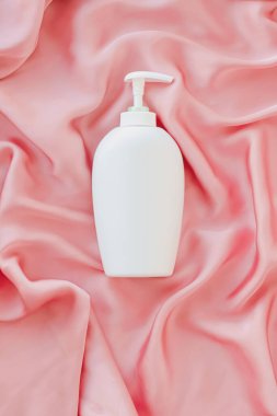 Pembe ipek arka planda ürün modeli olarak boş etiket kozmetik kutu şişesi