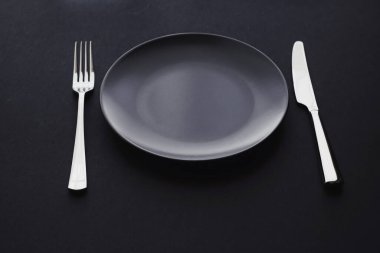 Siyah arka planda boş tabaklar ve gümüş takımlar, bayram yemeği için özel sofra takımı, minimal tasarım ve diyet