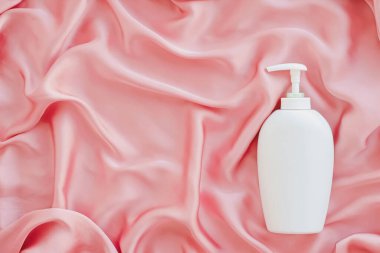 Pembe ipek arka planda ürün modeli olarak boş etiket kozmetik kutu şişesi