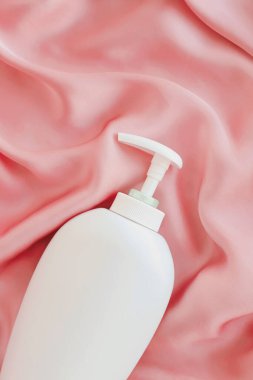 Pembe ipek arka planda ürün modeli olarak boş etiket kozmetik kutu şişesi