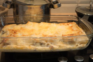 Masanın üzerinde fırında taze lazanya olan cam mutfak kabı.