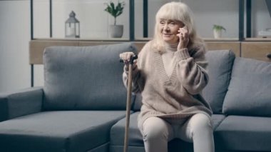 Kanepede akıllı telefondan konuşan kıdemli bir kadın.