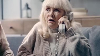 Bunamış yaşlı bir kadın kocasının yanında telefonla konuşuyor.