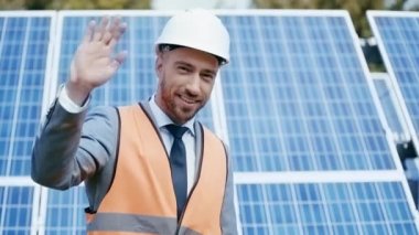 İş adamı el sallıyor, güneş panelini işaret ediyor. 