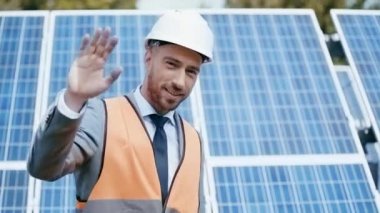 İş adamı el sallıyor, güneş panelini işaret ediyor. 