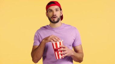 Adam film izliyor ve sarı üzerine izole edilmiş patlamış mısır yiyor.