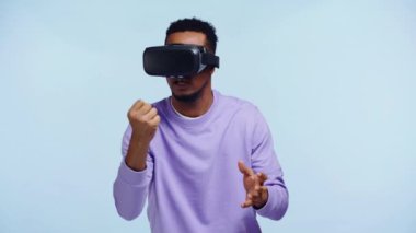 VR kulaklıkla hareket eden Afro-Amerikan bir adam mavi üzerine izole edilmiş.