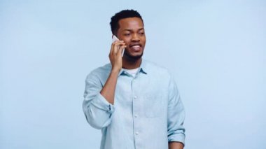 Gülümseyen Afrikalı Amerikalı adam mavi telefondan konuşuyor.