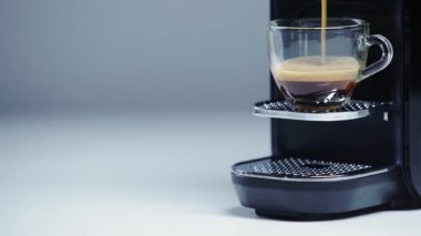 Kahve makinası beyaz ve gri bardağa kahve dolduruyor.