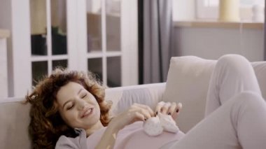 pregnant woman lying on sofa with baby shoes and touching belly