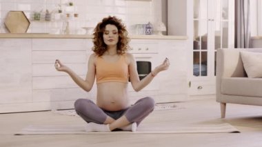 pregnant woman meditating in lotus pose at home on yoga mat